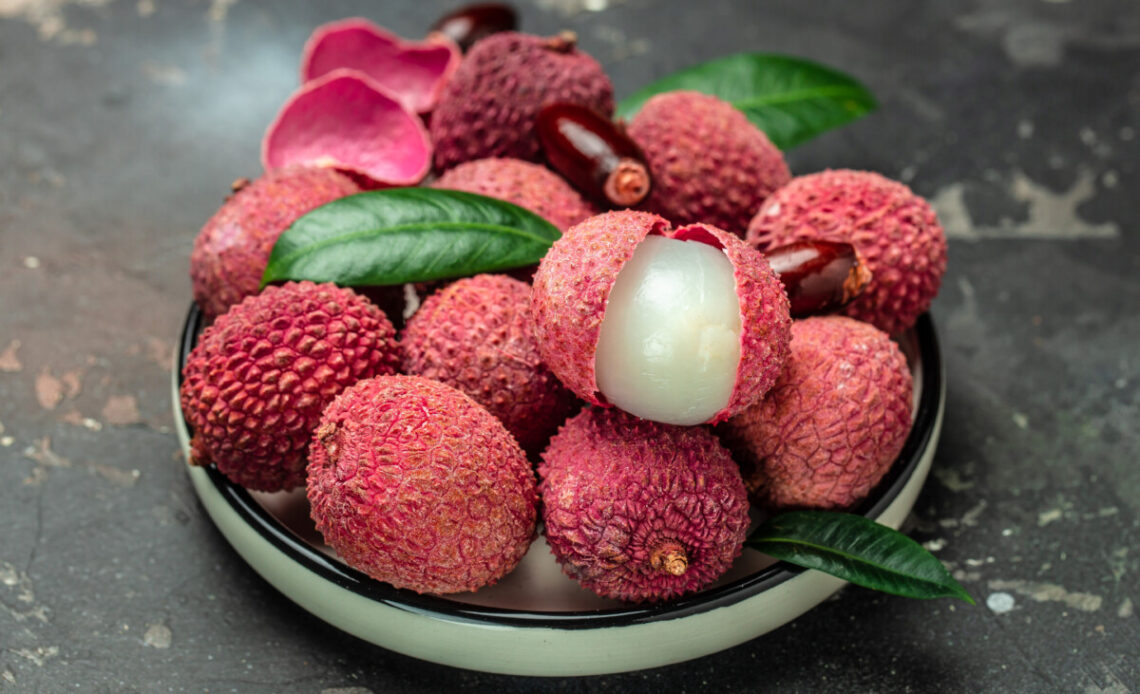 Juicy Lychee with cut in half and leaves on plate on a dark background, top view